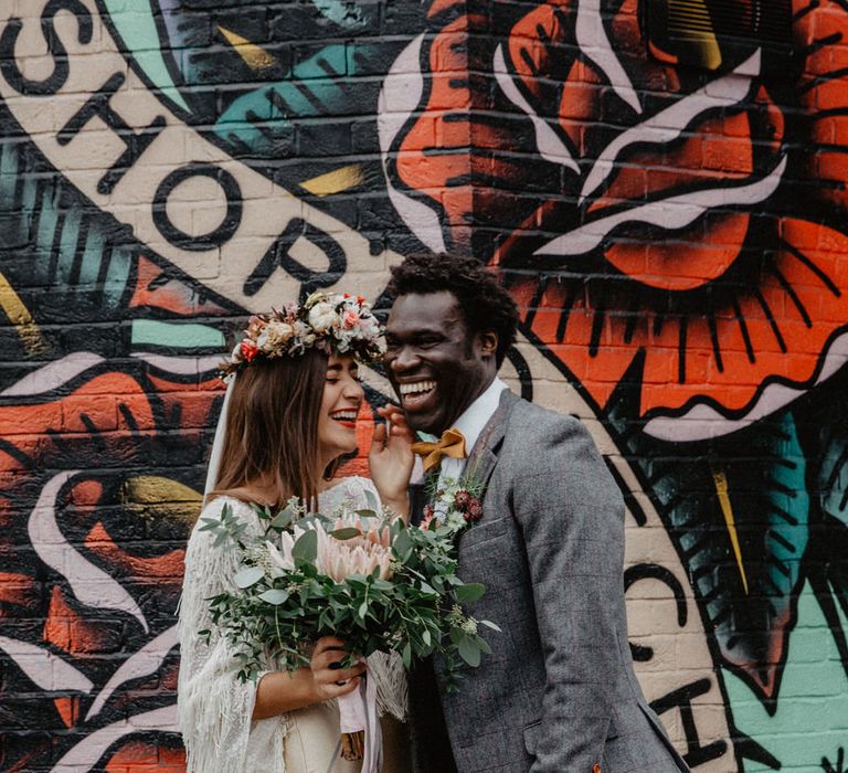 Couple stand together in front of London wedding photo location Shoreditch graffiti wall laughing together