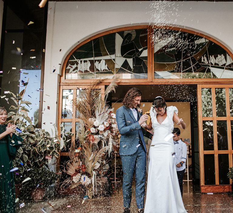 Confetti moment with bride in a ruffle sleeve Rime Arodaky wedding dress and groom in a navy blue three-piece suit