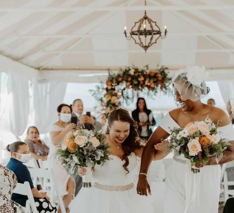 Extremely happy brides walking down the aisle holding orange, peach and coral wedding bouquets after being pronounce wife and wife