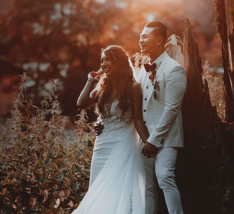 Asian bride & groom stand together outdoors with sunlight behind them