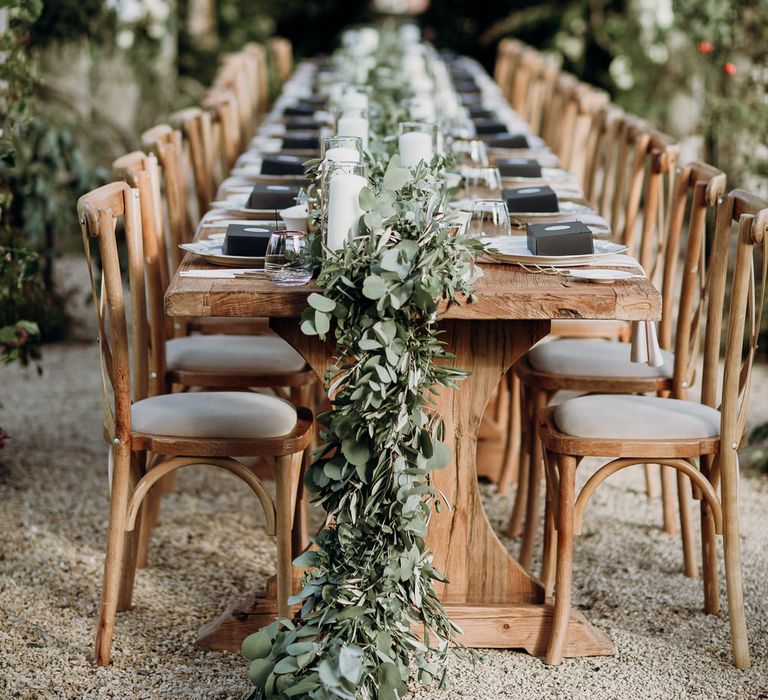 Rustic wooden wedding table with light wooden chairs and wedding table garland under canopy of foliage at Euridge Manor wedding