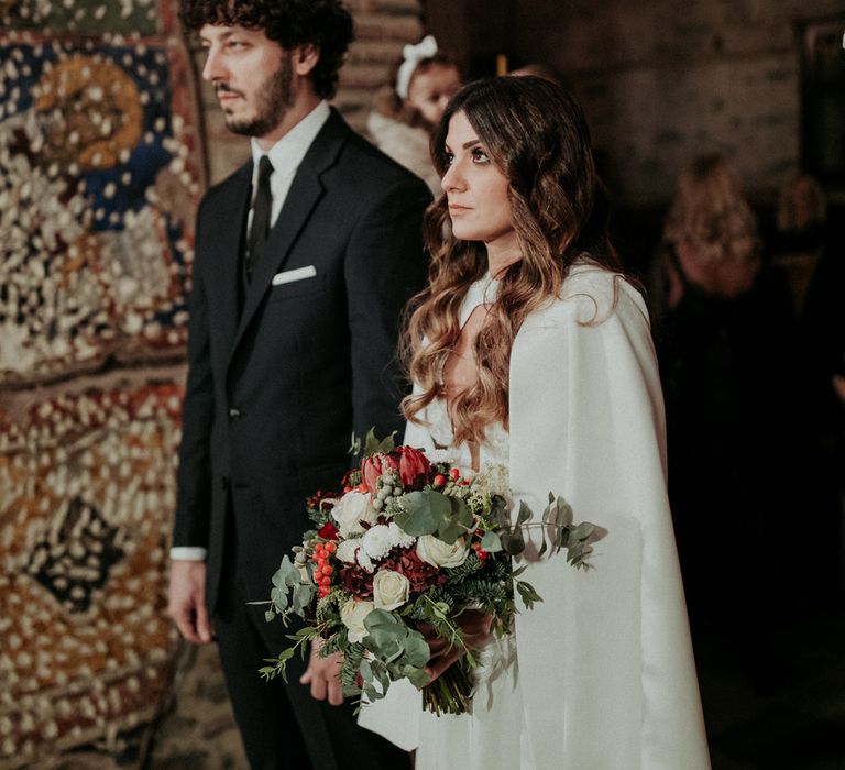 The bride and groom a their church ceremony, the bride is wearing a Nadia Rapti gown and wedding cape