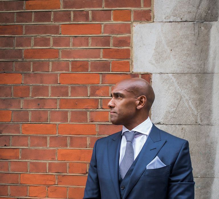 Stylish groom in a navy three-piece suit with light blue pocket square and patterned tie 