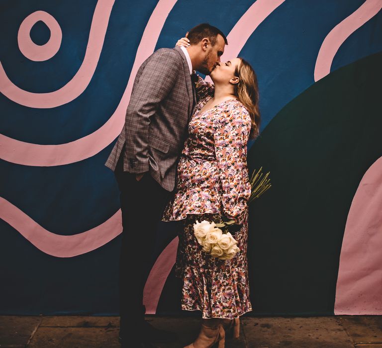 Bride & groom kiss in front of wall painted with pink and blue stripes