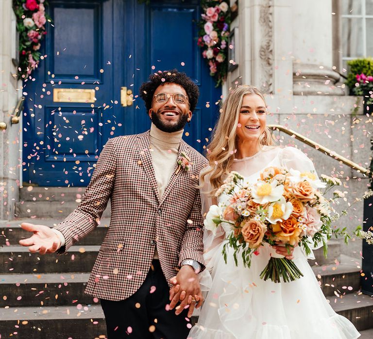 Confetti moment for stylish Chelsea wedding with bride and groom in patterned blazer and short wedding dress