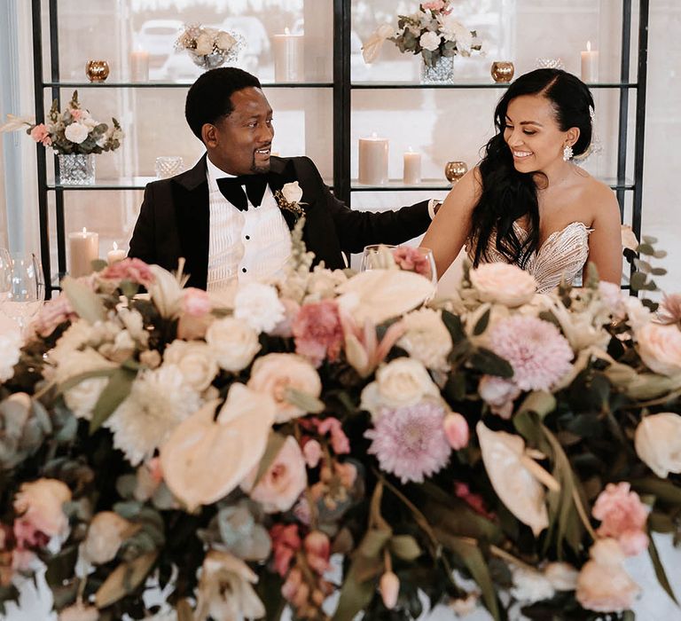 Bride and groom sitting at their sweetheart table with pink and white floral arrangement and candles 