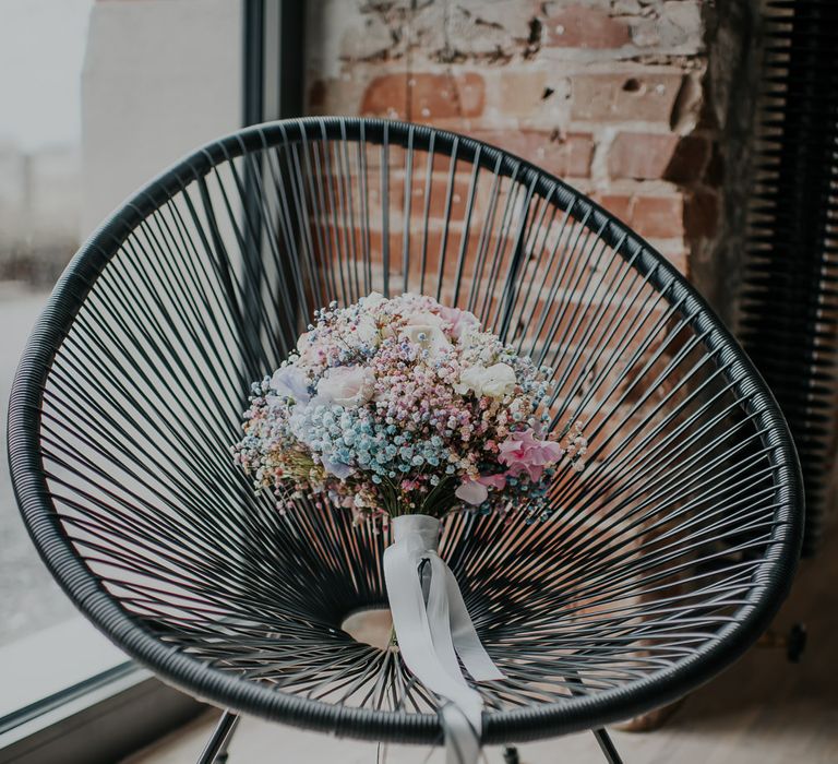 Pastel gypsophila wedding bouquet wrapped in white ribbon resting on a black wire chair 