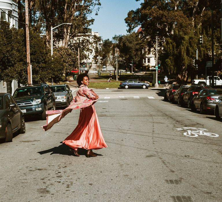 Bride in a coral dress and patterned coat twirling in the road at San Francisco engagement session 