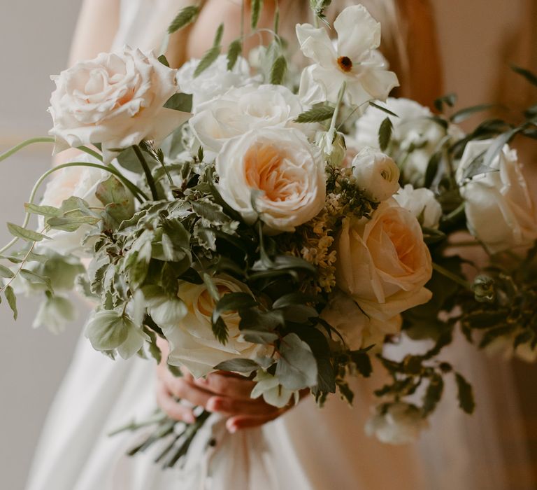 Bride holds large white floral bouquet filled with white roses and green foliage