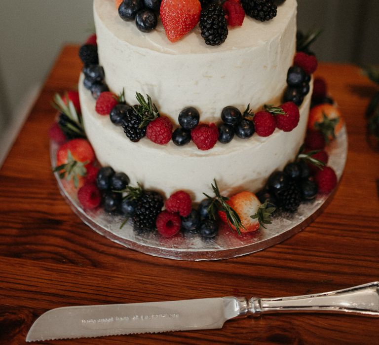 Two tier iced white wedding cake with mixed berries and cute cartoon animal cake toppers