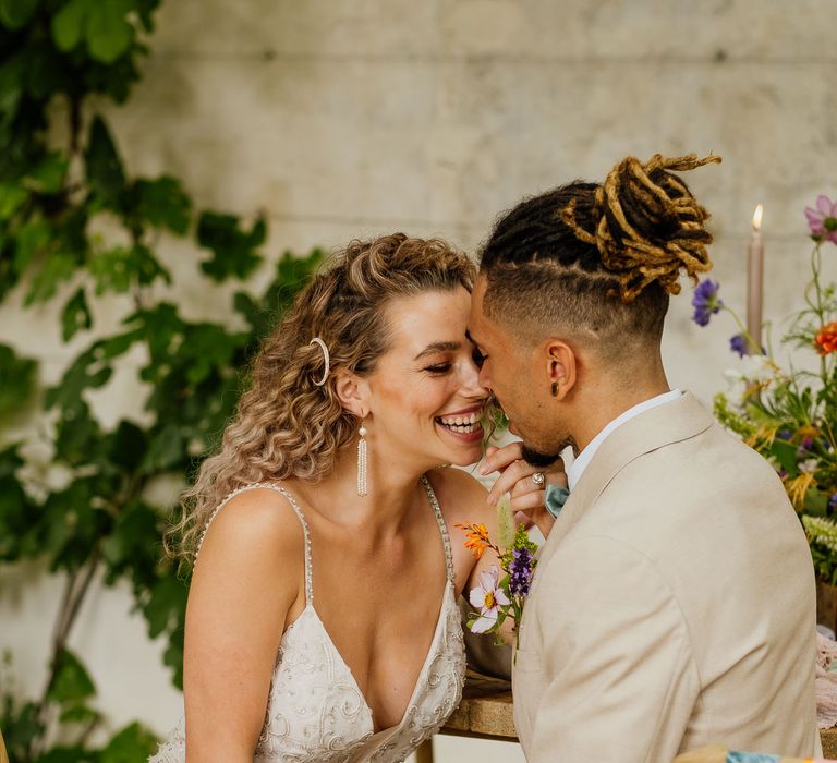 Groom in a beige suit holding hands with his curly haired bride in an embellished wedding dress