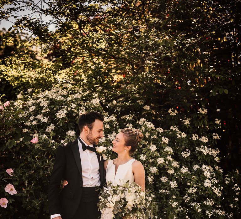 Bride & groom kiss outdoors as bride holds white bouquet of flowers tied with green ribbon