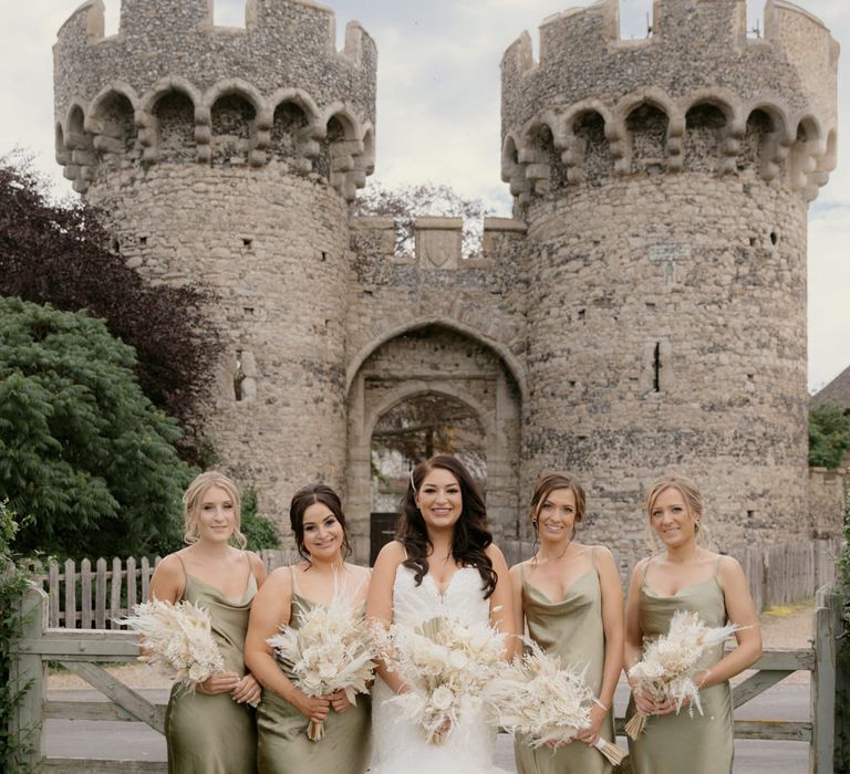 Bridal party portrait in front of Cooling Castle Barn wedding venue in green satin bridesmaid dresses and fishtail wedding dress