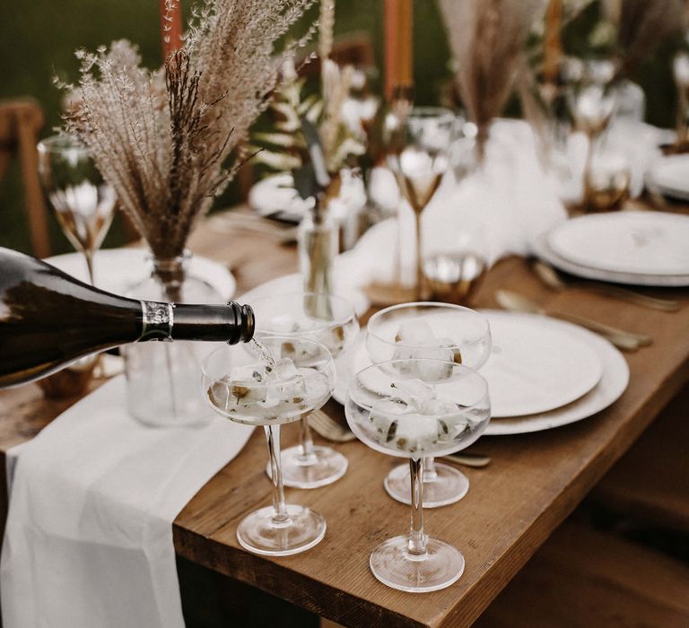 Champagne being poured into coupe glasses with ice cubes 