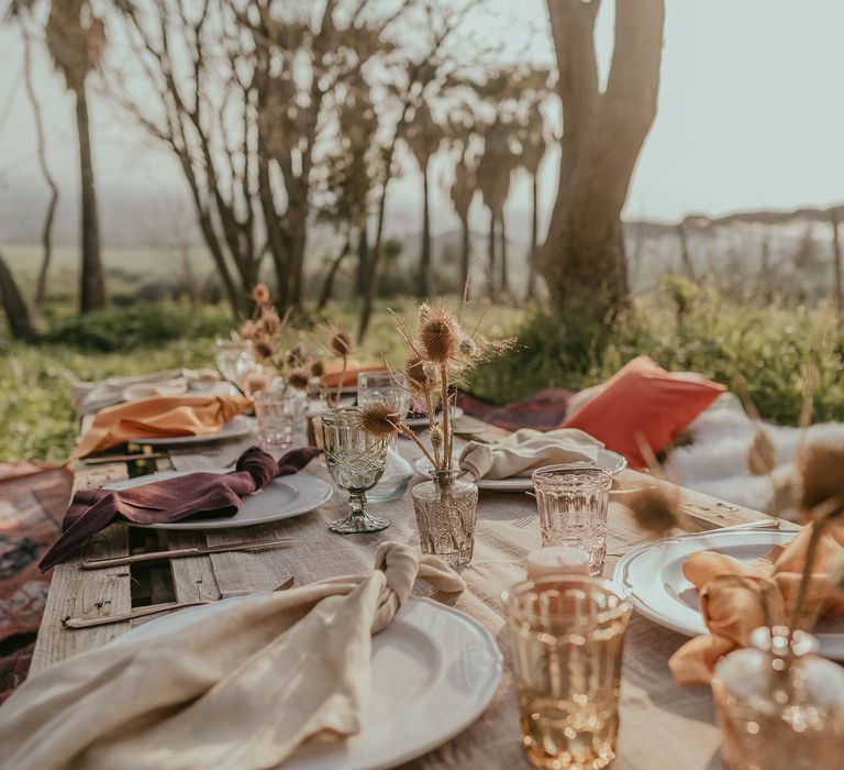 Rustic wooden palette reception table complete with Moroccan style rugs for sitting and dried floral decor set in small crystal orange coloured vases and fabric napkins