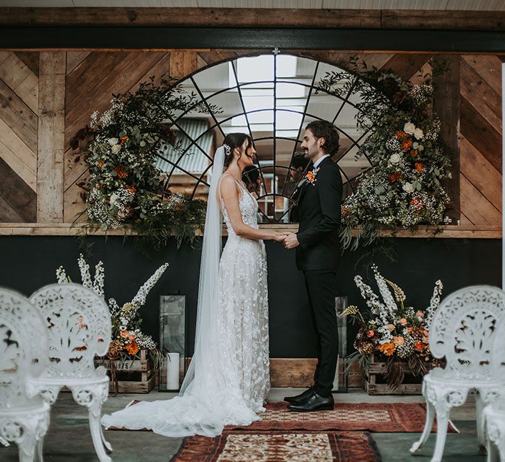 Bride in an appliqué wedding dress and cathedral length veil holding hands with her groom in a tuxedo at new Lake District wedding venue, Ghyll Barn 