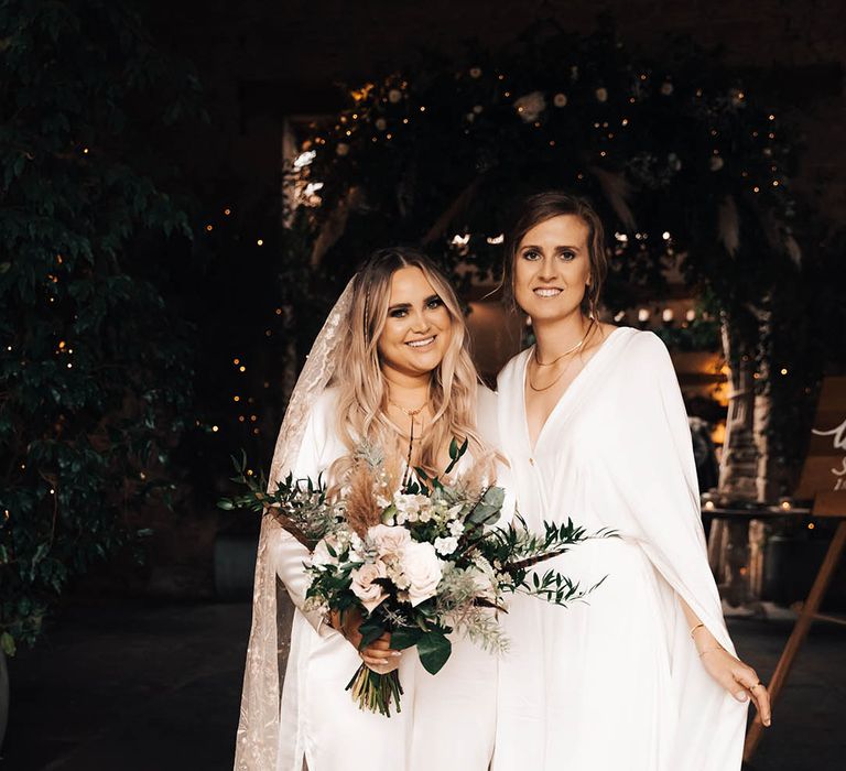 Blonde bride carries white floral bouquet with green foliage