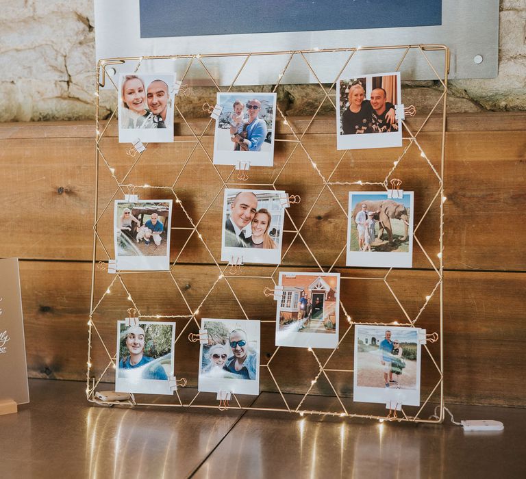 Gold wire frame with lights and polaroids next to frosted acrylic wedding sign with quote at Tythe Barn wedding with barn wedding flowers