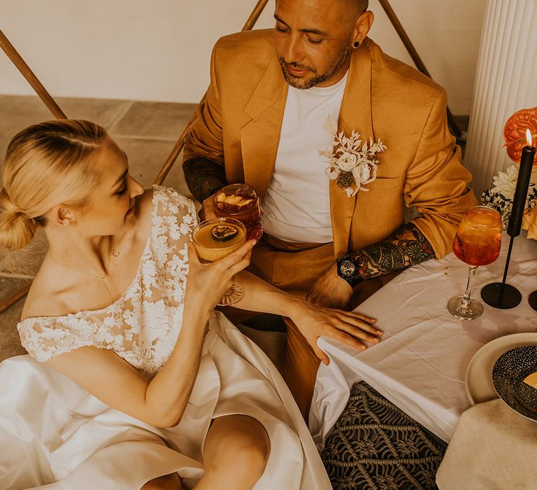 Groom in a mustard suit and bride in a lace Bardot bodice wedding dress sipping signature cocktails 