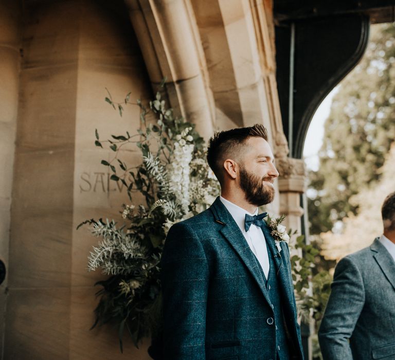 Groom in check suit waits for his bride at outdoor wedding ceremony