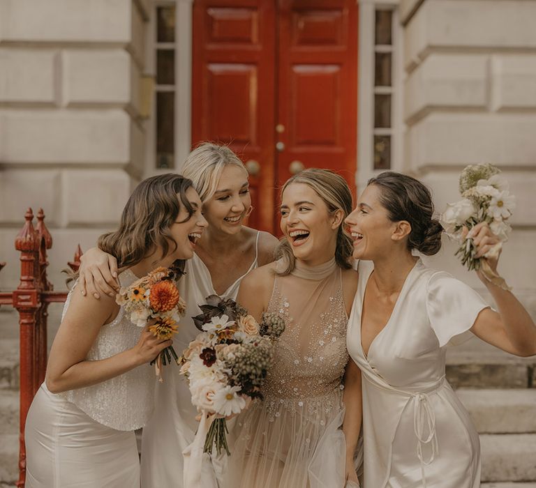 Bride in a tulle halter neck wedding dress and bridesmaids in white satin dresses standing on the steps at Clerkenwell House 