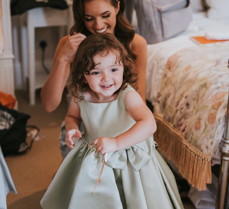 Flower girl in green satin dress with bow with laughing bride in floral headband before summer wedding at Primrose Hill Wedding