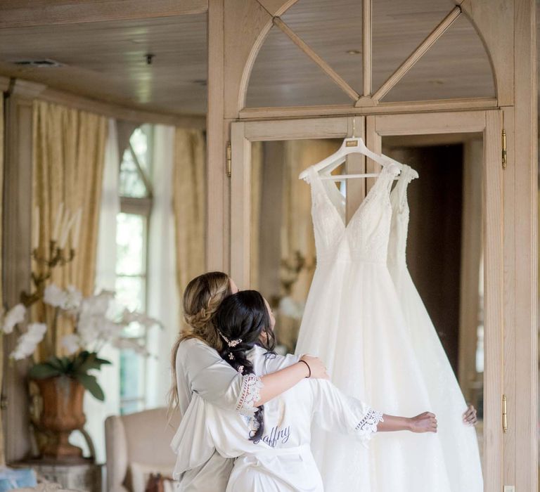 Bride looks at her wedding gown as bridesmaid holds her arm around her shoulders