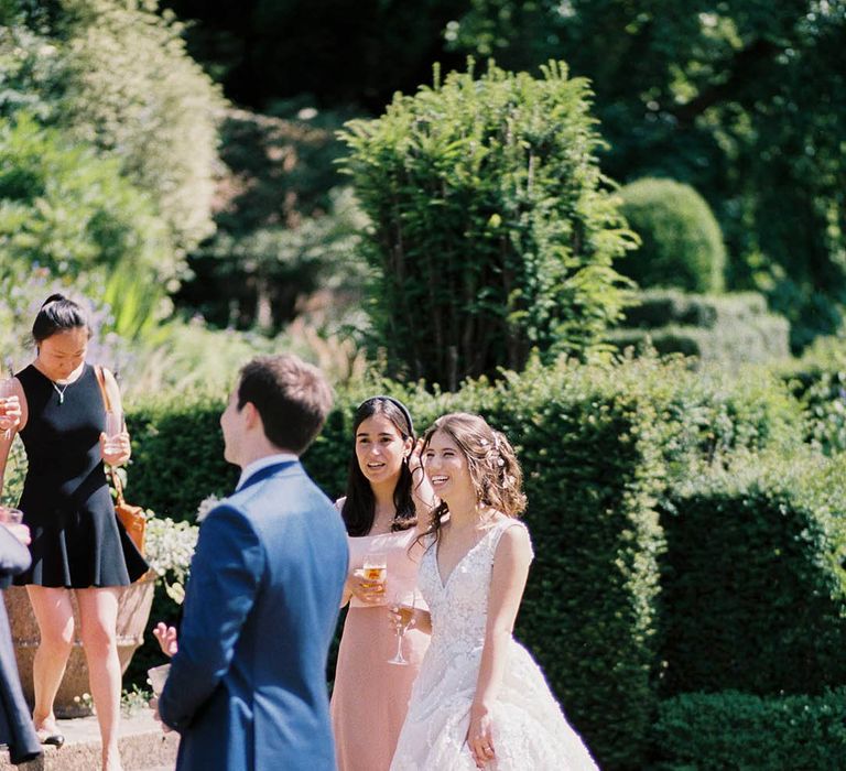 Bride laughs with wedding guests as she holds champagne outdoors on her wedding day