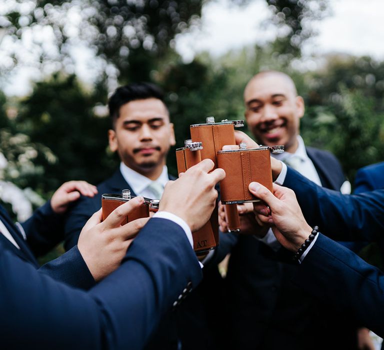 Groomsman party in navy suits having a tipple with their leather designed hip flasks