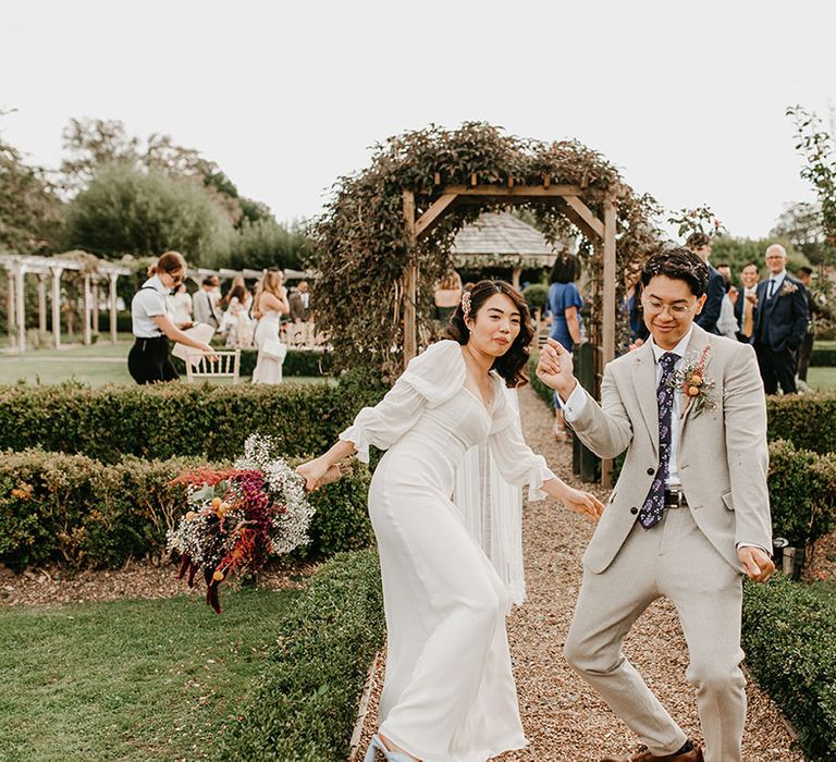 Bride & groom dance down garden pathway with one another after wedding ceremony