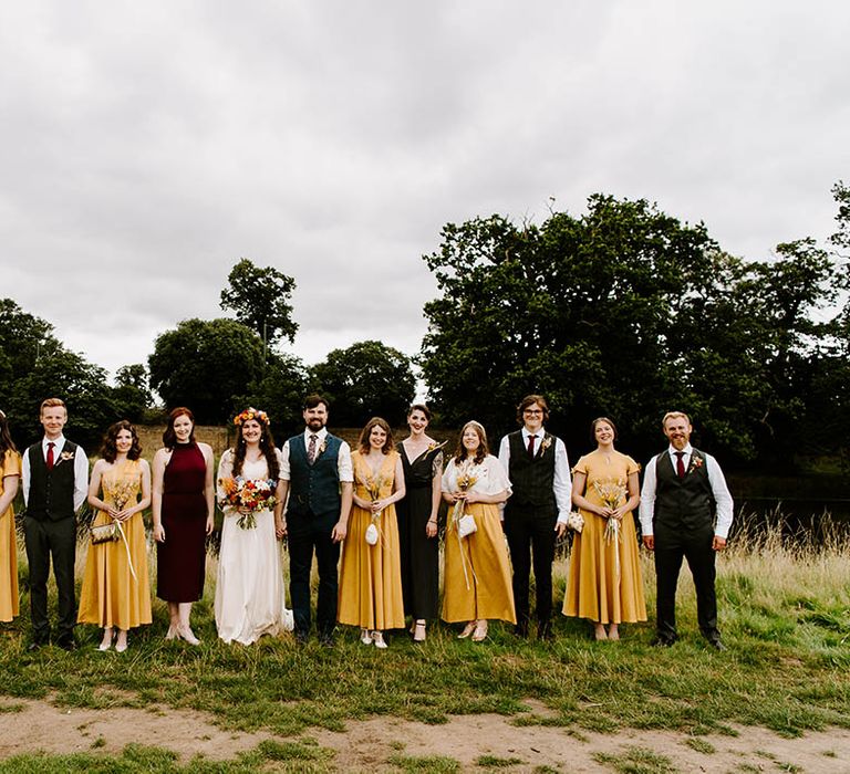 Bride & groom stand with their wedding party outdoors 