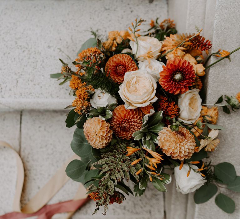 Orange and peach dahlia and rose wedding bouquet with foliage 