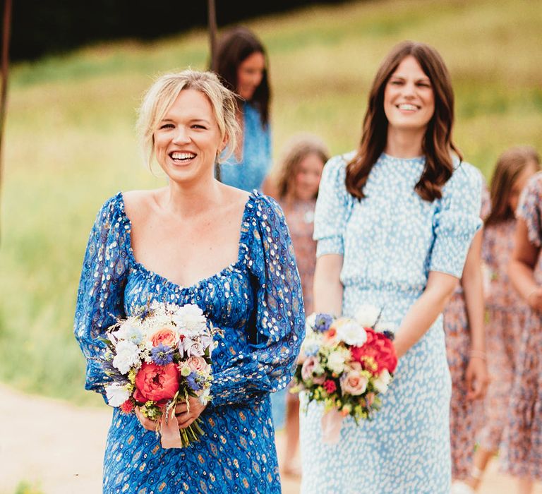 Bridesmaid wears blue floral gowns as they hold colourful bouquets