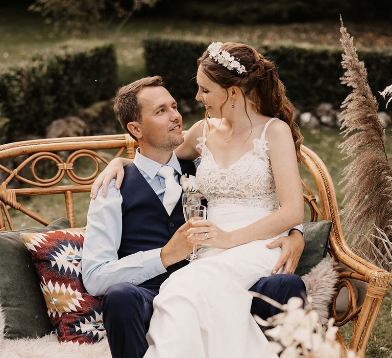 Bride sits on her grooms lap outdoors on their wedding day