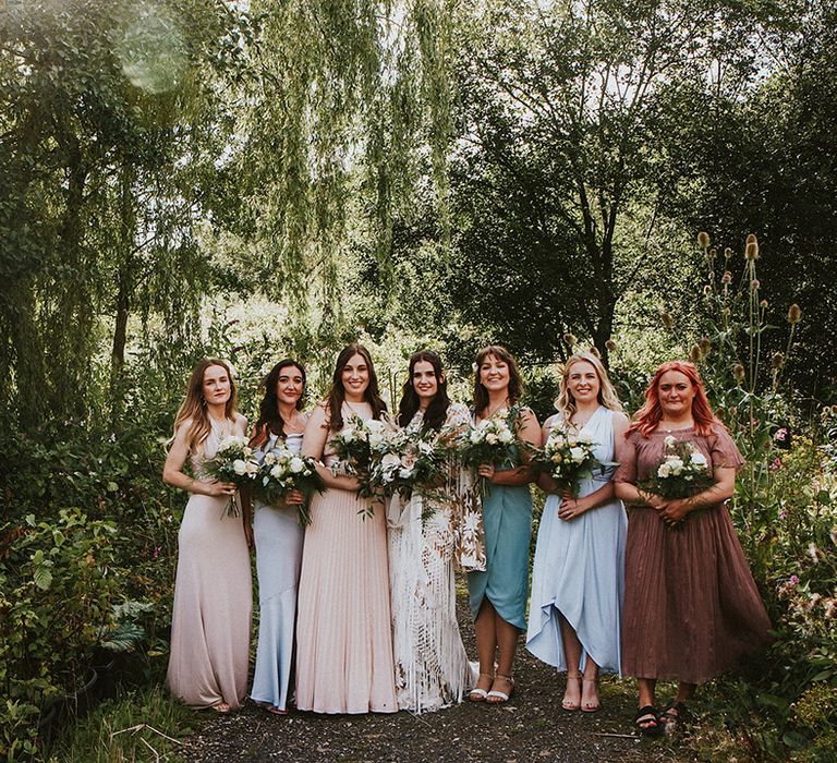 Bride stands with her bridesmaids who wear mismatched bridesmaids gowns