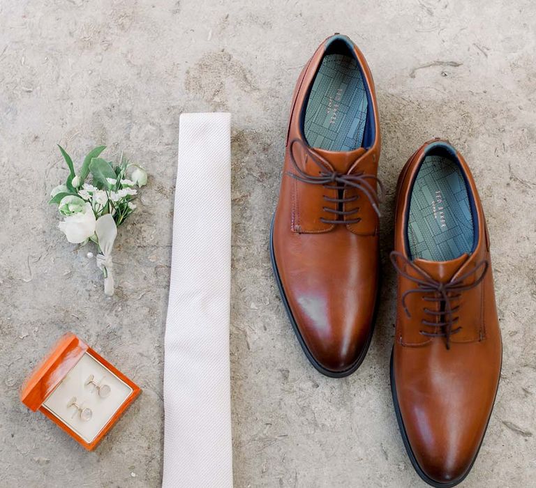 Mens wedding shoes next to cufflinks and floral buttonhole 