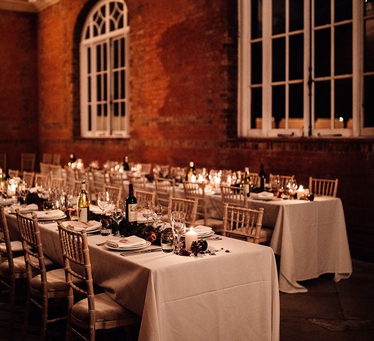 Long tables set with white table clothes, tall wine glasses with foilage and candles 