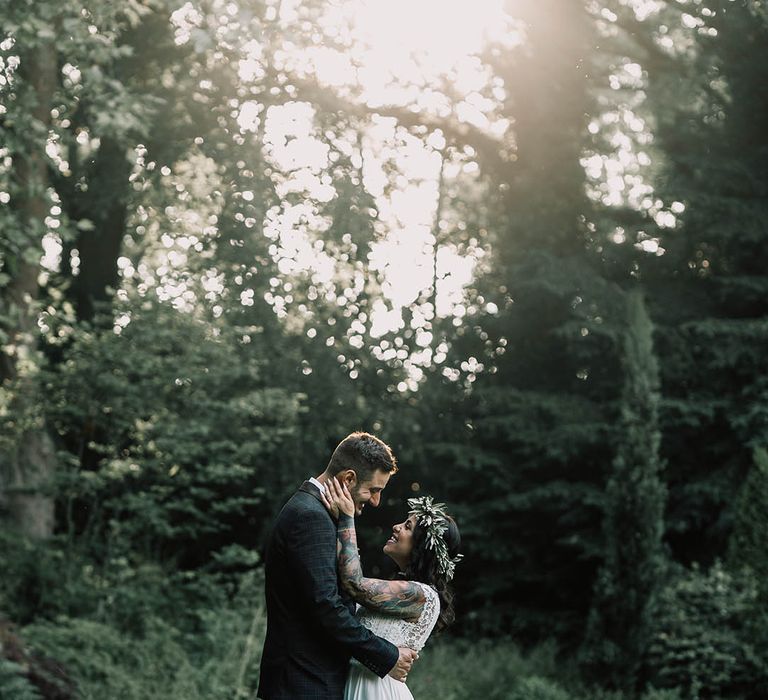 Bride & groom look lovingly at one another as the sun shines through the trees 