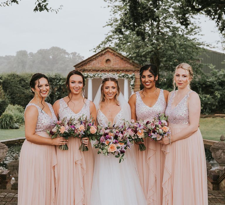 Bride in tulle wedding dress with bridesmaids in blush pink dresses with sequinned tops at country house venue