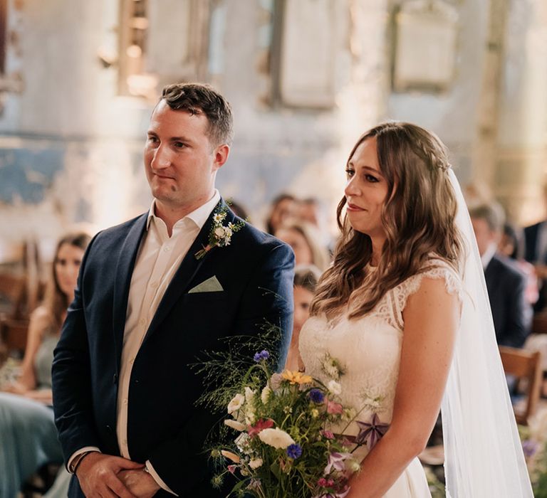 Bride in two piece wedding top and skirt and braided hairstyle and groom in navy blue suit jacket and wildflower boutonnière