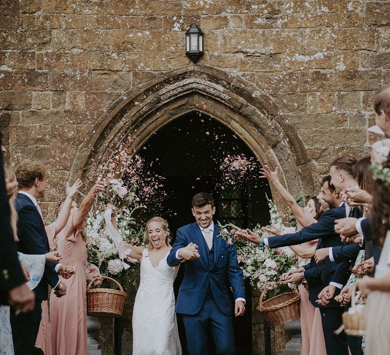 Bride and groom walk out of the church ceremony wedding into a confetti exit from the wedding guests 