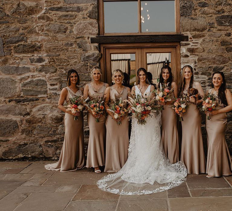 Bride in flower lace skirt wedding dress and matching veil stands with bridesmaids in gold satin dresses