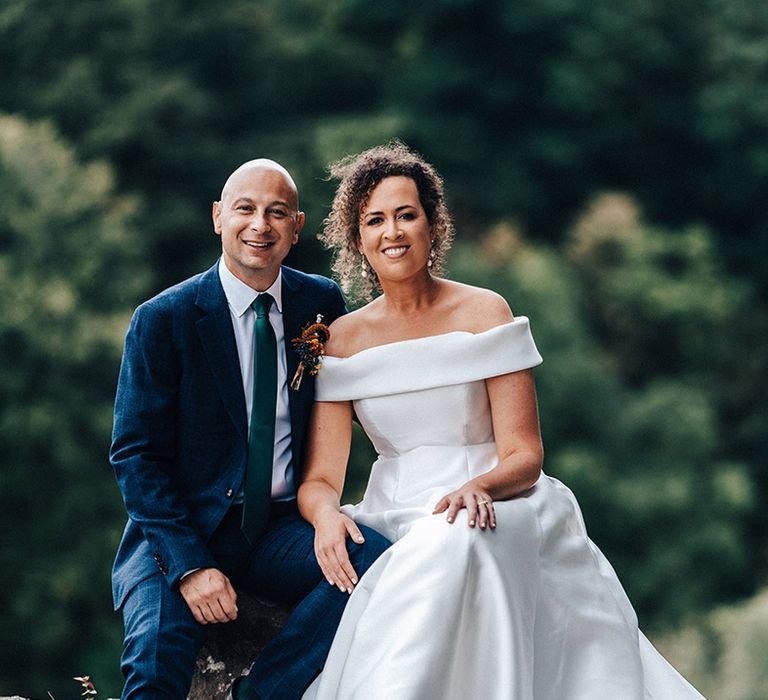 Bride in off the shoulder pleated wedding dress with groom in blue checkered suit and green tie 