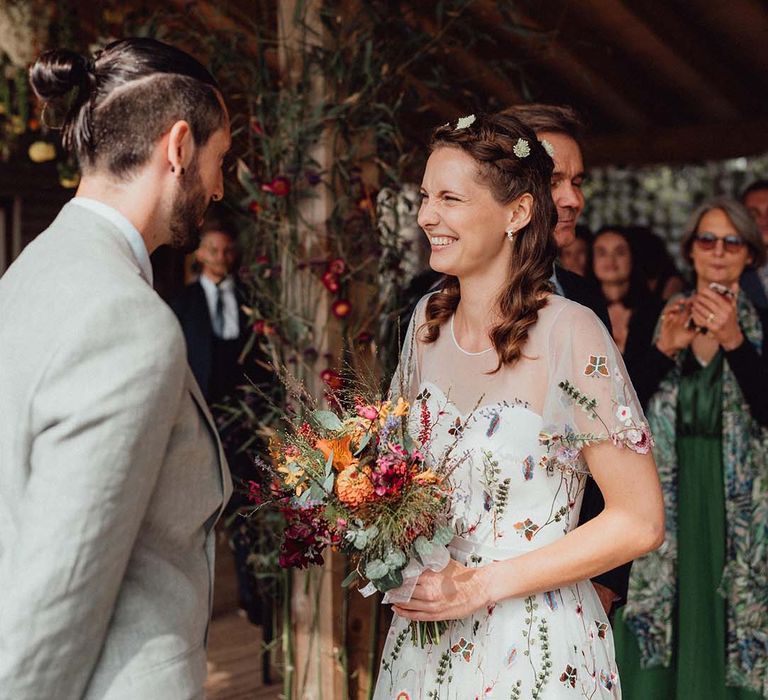 Smiling bride in flower embroidery dress with flower hair accessories and colourful wedding bouquet 