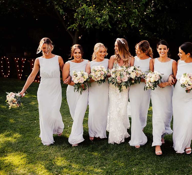 Bridal party with seven bridesmaids in grey high neck low back dresses with bride in lace wedding dress holding pink and white bouquets