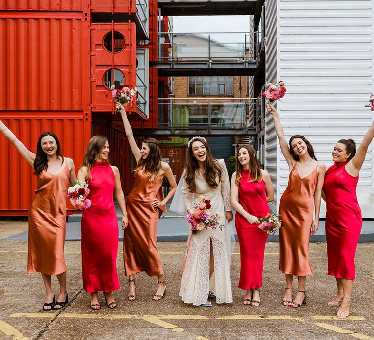 Bride poses with her bridesmaids as they lift their bright and colourful pink wedding bouquets into the air