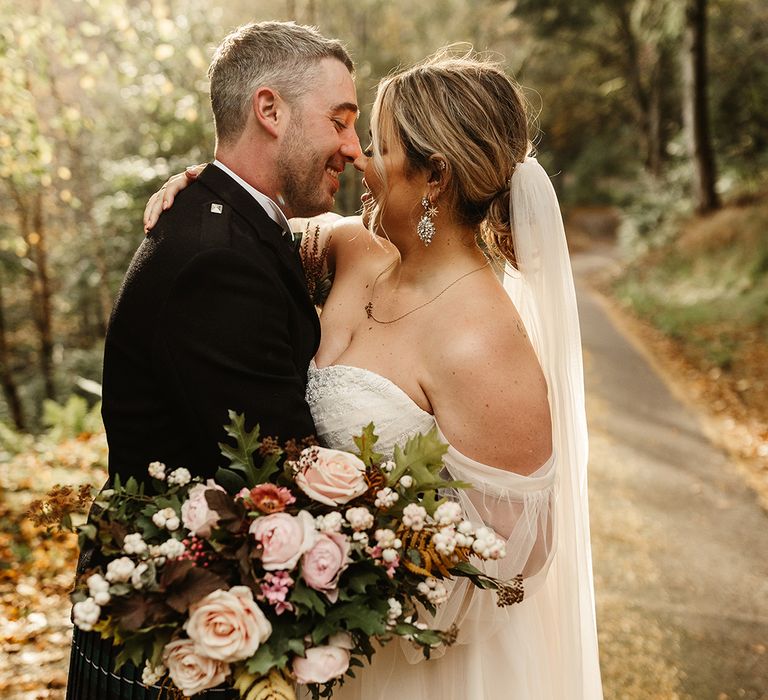 Bride and groom lean in for a kiss as they stand outside together on sunny autumn day 