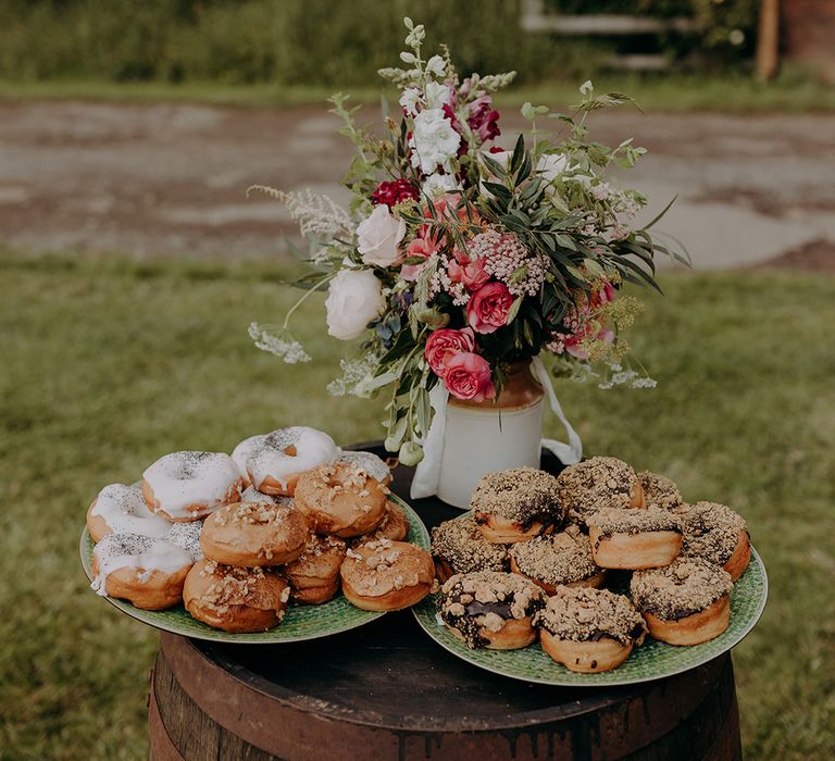 Pink, red and white wedding flowers next to plates of yummy doughnuts for guests