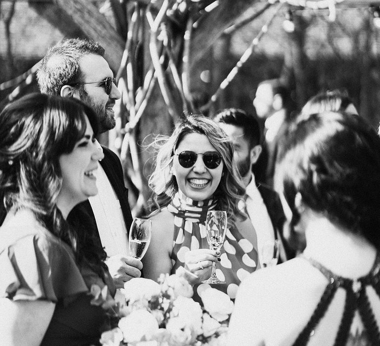 Wedding guests socialise together with drinks wearing sunglasses