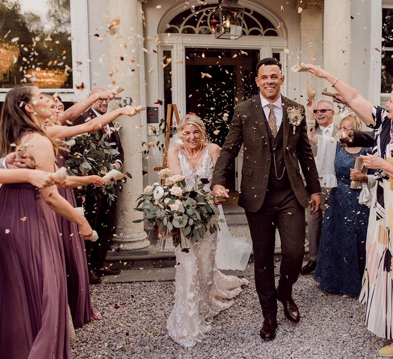 Groom in checkered brown suit walks out from the ceremony with bride in 3D lace Made With Love Bridal gown